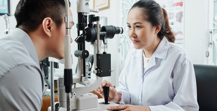 Asian female optometrist looking through the special medical equipment and examining her patient's eyesight at hospital